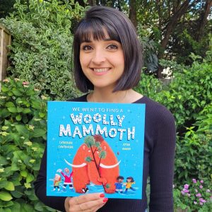 Illustrator Aysha Awwad holding a copy of her new book Woolly Mammoth in front of her.